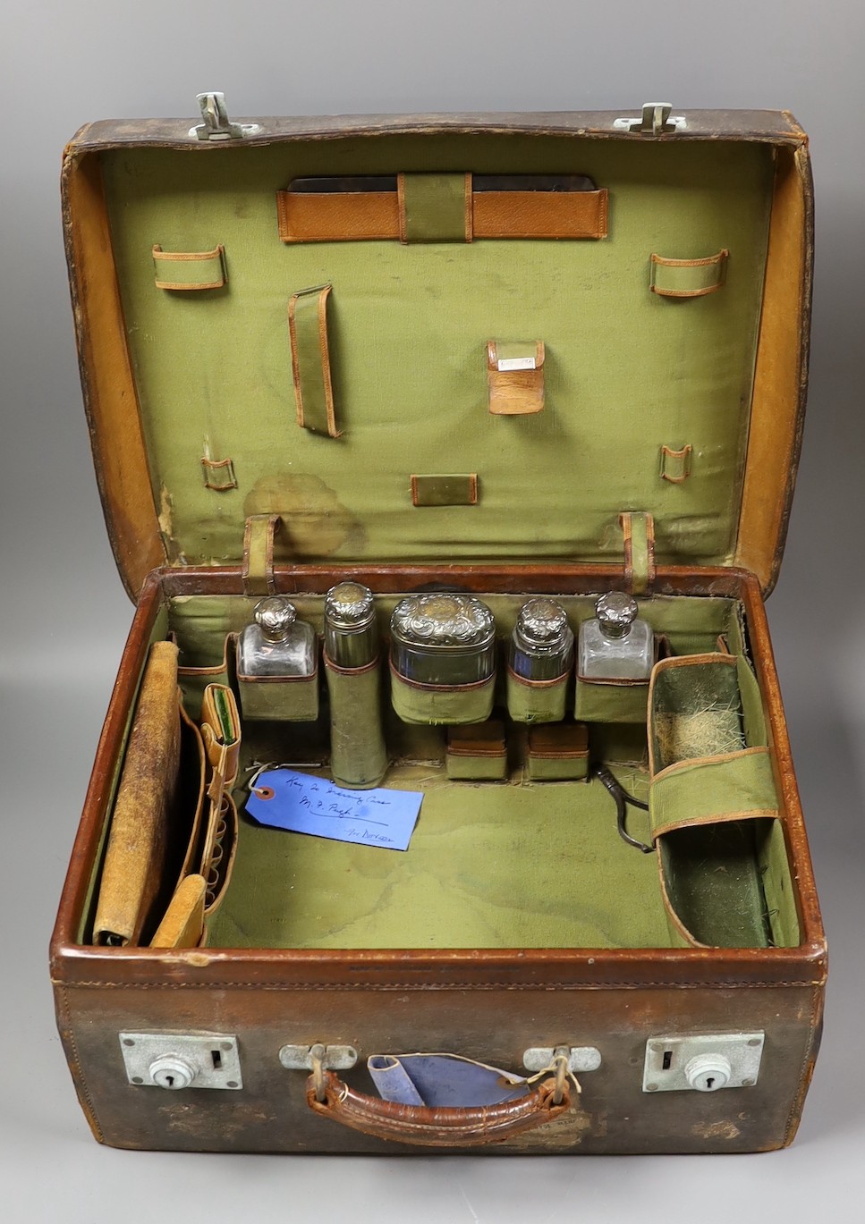 A late Victorian leather travelling vanity case containing five repousse silver topped glass toilet jars, 43.8cm.